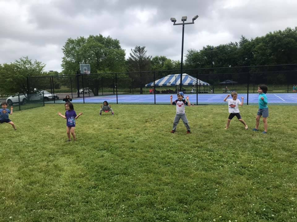 Campers running on the grass with the sports court behind them