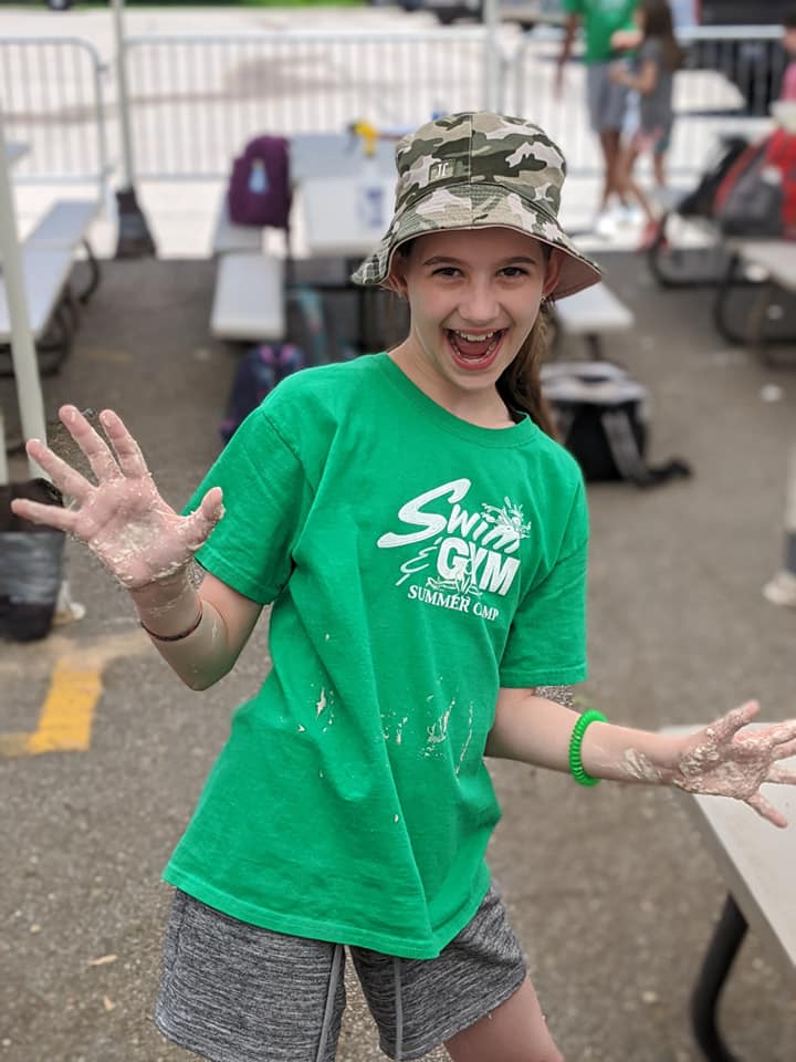 Camper showing a paint-covered hand in a Swim&Gym Summer Camp shirt